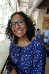 Valerie, an African American woman, smiles for the camera while sitting in a coffee shop